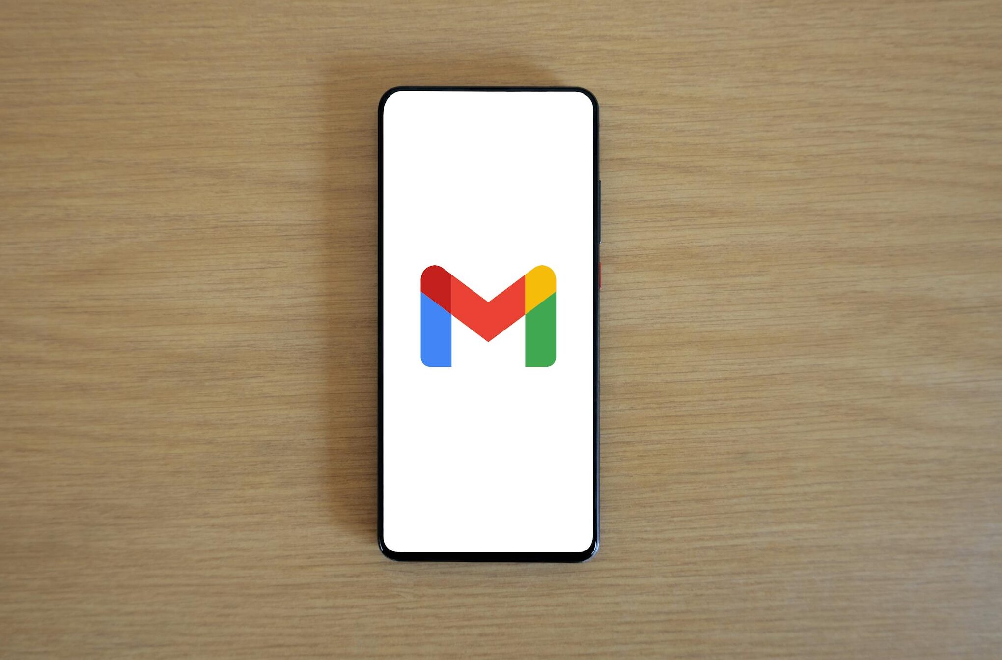 A smartphone displaying the Gmail app logo on a wooden surface, viewed from above.